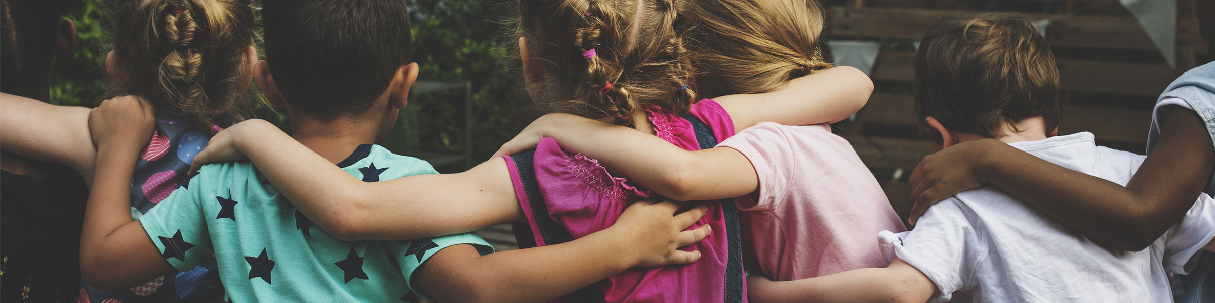 Rear view of children in a group hugging